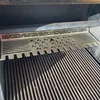 A close-up view of a stainless steel grill accessory with a cutout design, placed over a grill grate. Podgląd zdjęcia produktu