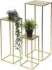 Three gold metal plant stands of varying heights, each with a square top and base, are displayed against a white background. Two of the stands hold artificial plants. Náhled obrázku produktu