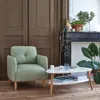 A living room scene with a green armchair and a white coffee table in front of a fireplace. Náhled obrázku produktu