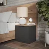 A bedside table next to a bed, with a lamp and books on top. Náhled obrázku produktu