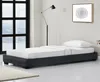 A minimalist bedroom setting with a single bed, a floor lamp, and a framed artwork on the wall. Produktbild-Vorschau