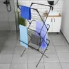 A black metal drying rack with several towels hanging on it, placed in a modern bathroom with tiled floors and a white vanity with a sink. Náhľad obrázku produktu