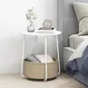 A white round side table with a storage basket underneath, placed next to a bed. Anteprima dell’immagine prodotto