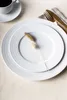 A white dinner plate with a decorative sprig on top, set on a light beige tablecloth. Produktbild-Vorschau