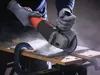 A person wearing gloves is using an angle grinder to cut a tile. Produktbild-Vorschau