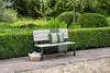 A garden bench with cushions and a blanket in a lush garden setting. Produktbild-Vorschau
