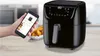 A hand holding a smartphone displaying an air fryer app next to a black air fryer and a bowl of food. Produktbild-Vorschau