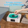 A hand is placing a stylus on a vinyl record on a white turntable, which is on a wooden table. Produktbild-Vorschau