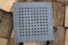 A square cast iron grate with many circular holes is placed on a pile of chopped wood. Produktbild-Vorschau