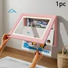 A person is inserting artwork into a pink, wall-mounted picture frame designed for children's art. Produktbild-Vorschau