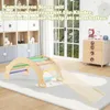 A wooden climbing arch with a slide is set up on a rug in a child's room, with shelves and a window in the background. Produktbild-Vorschau