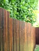 A close-up view of a bamboo fence with green foliage in the background. Produktbild-Vorschau