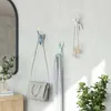 Three decorative hooks shaped like climbing figures are mounted on a light-colored wall, holding a handbag, a scarf, and a necklace. Náhled obrázku produktu