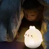 A child is under a blanket with a glowing bunny-shaped night light. Produktbild-Vorschau