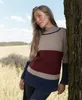 A woman leans against a tree in a field, wearing a striped sweater. Produktbild-Vorschau