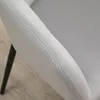 A close-up view of a light gray upholstered chair armrest with visible stitching and a dark leg in the background. Voir les images du produit