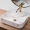 A close-up shot of a marble-patterned sink with a gold faucet and drain, placed on a wooden surface. Produktbild-Vorschau