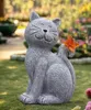 A gray cat statue with an orange butterfly on its tail, sitting on green grass in a garden. Produktbild-Vorschau