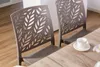 Two taupe chairs with a leaf pattern on the backrests are placed next to a wooden table. A white teacup and saucer are on the table. Anteprima dell’immagine prodotto