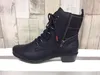 A black boot with a plaid shaft sits on a white surface against a wood-paneled background. Voir les images du produit