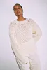 A woman wearing a cream-colored knitted sweater and cream-colored pants, posing against a white background. Produktbild-Vorschau