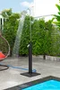 An outdoor shower is running next to a swimming pool, surrounded by greenery. Produktbild-Vorschau