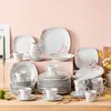A collection of white porcelain dinnerware with pink floral accents, arranged on a wooden surface against a light pink background. Voir les images du produit