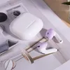 A white charging case and two purple and white earbuds are arranged on a light-colored surface. Voir les images du produit
