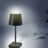 A modern table lamp with a black shade and base is placed on a white surface next to an open book. The lamp is illuminated, casting a soft glow. Produktbild-Vorschau