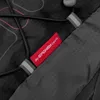 A close-up view of a red tag with white text on a black backpack. Produktbild-Vorschau