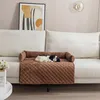 A dog bed cover is placed on the armrest of a sofa, with a stuffed dog on it. A framed abstract art piece hangs on the wall behind the sofa. Náhled obrázku produktu