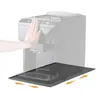 A hand is shown pressing on the top of a coffee machine, while a black drip mat is positioned in front of it, with arrows indicating it can be slid out. Produktbild-Vorschau