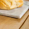 A close-up of a marble serving platter with a bread roll on it, placed on a wooden surface. Produktbild-Vorschau