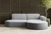 A modern, modular sectional sofa with rounded edges upholstered in corduroy fabric, set against a dark paneled wall with a potted plant and tree. Náhled obrázku produktu