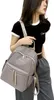 A woman wearing a black crop top and gray pants is modeling a gray backpack. Podgląd zdjęcia produktu
