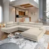 A modern U-shaped sectional sofa in a spacious, well-lit living room with a minimalist aesthetic. The sofa is the focal point, placed on an ornate rug in front of a kitchen area. Podgląd zdjęcia produktu