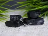 Several pieces of black resin are arranged on a textured white surface, with blurred green foliage in the background. Produktbild-Vorschau