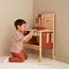 A young boy is playing with a wooden toy workbench in a room. Produktbild-Vorschau