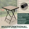 A square folding table with a wood-look top and black metal frame, set up on a patio or deck. There are some plants in the background. Anteprima dell’immagine prodotto