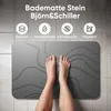 A person's feet are standing on a dark gray bath mat with a wavy pattern, placed on a tiled floor. Produktbild-Vorschau