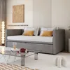 A modern living room with a gray sofa bed, a glass coffee table with decorative items, and a floor lamp. Produktbild-Vorschau
