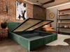 A bedroom with a green upholstered bed frame with the mattress support lifted, revealing storage space underneath. The room has a brick wall, wooden slatted wall paneling, a leather armchair, and a tall shelving unit. Produktbild-Vorschau