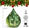 A green glass teardrop-shaped decorative light with a snowflake and deer pattern, shown with a festive garland of fir branches, red ornaments, and gold bows at the top. Measurement and product feature icons are also visible. Produktbild-Vorschau