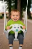 A smiling baby sitting in a swing with an elephant-shaped toy. Produktbild-Vorschau