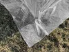 A close-up view of the corner of a white mesh greenhouse cover resting on dry grass. Anteprima dell’immagine prodotto
