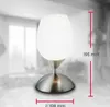 A table lamp with a frosted glass shade and a brushed metal base is shown in a room setting. Dimensions are indicated with measurement lines and text. Produktbild-Vorschau