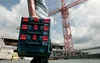 A person carrying a toolbox on a construction site with a crane in the background. Produktbild-Vorschau