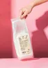 A hand holding a bag of white powder against a pink background. Produktbild-Vorschau