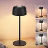 A black LED table lamp with a round base and a mushroom-shaped shade is shown on a wooden surface. The lamp is lit, casting a warm glow. Insets show the lamp in different lighting conditions. Produktbild-Vorschau