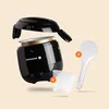 A black mini rice cooker with its lid open, floating above a light peach background. Accessories, a white rice paddle and a clear measuring cup, are also shown. Produktbild-Vorschau